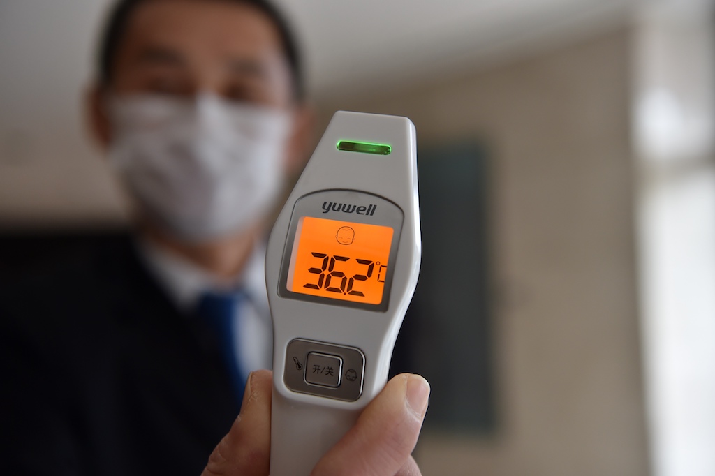 A hotel employee shows a temperature reading as he stands by the entrance to check all guests and anyone who enters the building to check for signs of the virus in the city of Wuhan